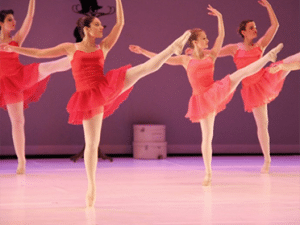 Groupe de danseuses classiques en costume rose réalisant un grand battement sur scène