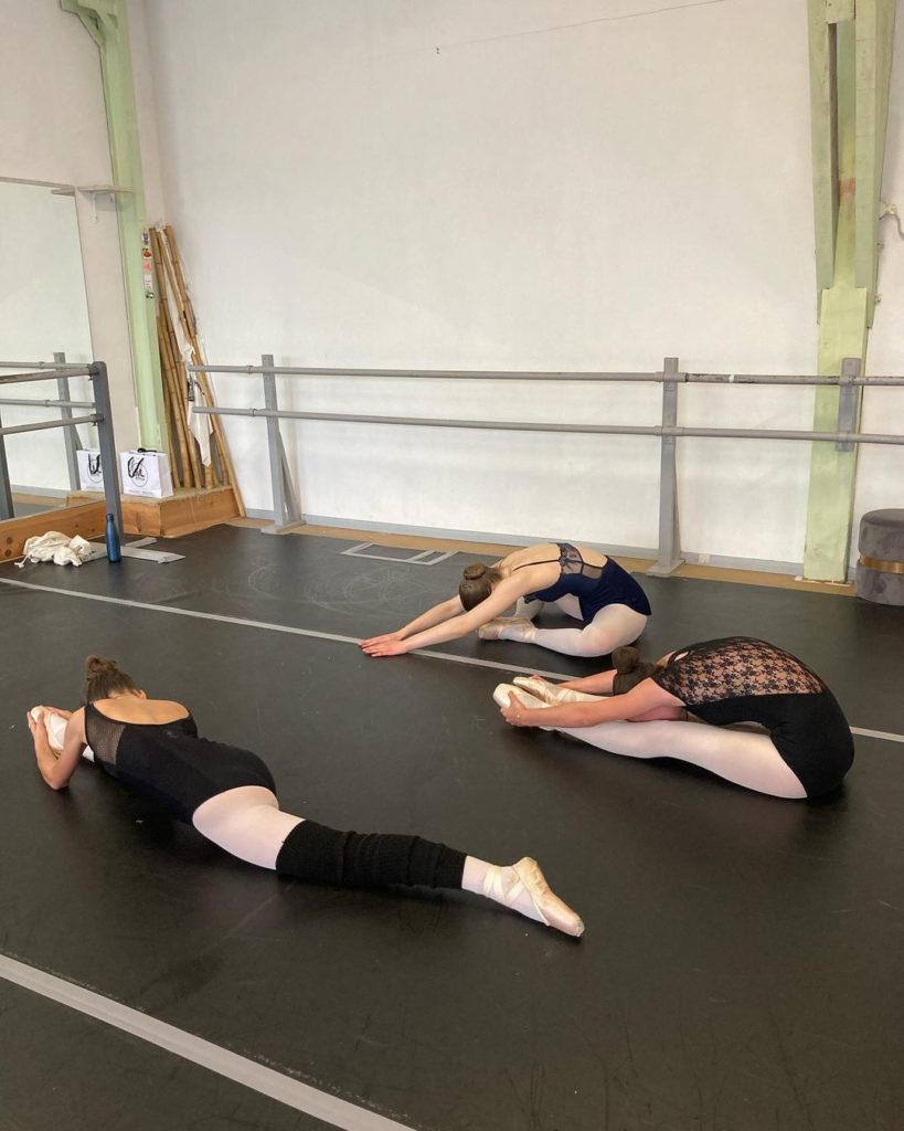Trois danseuses classiques en plein étirement au sol dans un studio de danse